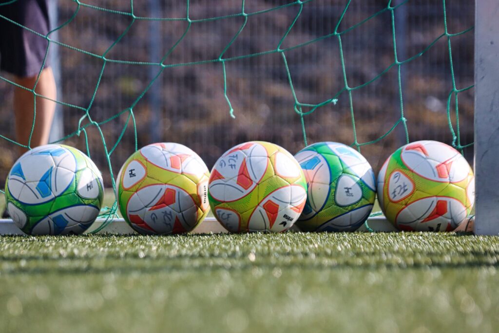 Ein paar Fußbälle, vor einem Fußballtor mit zerrissenem Netz