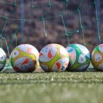 Ein paar Fußbälle, vor einem Fußballtor mit zerrissenem Netz