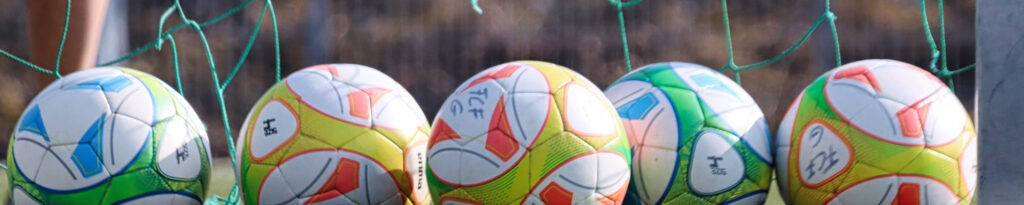 Ein paar Fußbälle, vor einem Fußballtor mit zerrissenem Netz