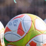 Ein paar Fußbälle, vor einem Fußballtor mit zerrissenem Netz