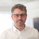 Porträt Florian Haase, junger Mann mit grauen Haaren, weißen Hemd und Brille