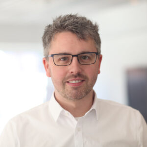 Porträt Florian Haase, junger Mann mit grauen Haaren, weißen Hemd und Brille