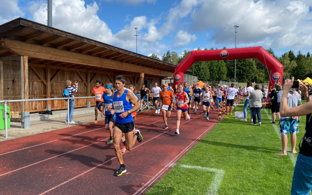 Der Start bei Grasbrunner Lauf 2024 mit vielen Kindern und Erwachsenen auf einer Kunststoffbahn, dazu ein aufgeblasenes Banner