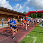 Der Start bei Grasbrunner Lauf 2024 mit vielen Kindern und Erwachsenen auf einer Kunststoffbahn, dazu ein aufgeblasenes Banner
