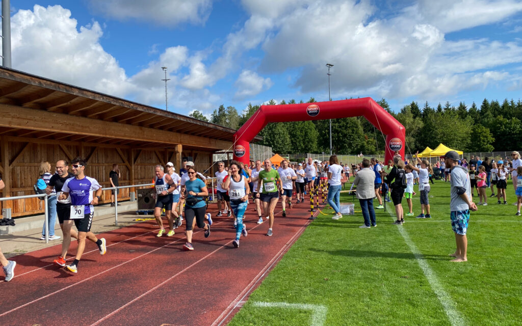 Der Start bei Grasbrunner Lauf 2024 mit vielen Kindern und Erwachsenen auf einer Kunststoffbahn, dazu ein aufgeblasenes Banner