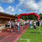 Der Start bei Grasbrunner Lauf 2024 mit vielen Kindern und Erwachsenen auf einer Kunststoffbahn, dazu ein aufgeblasenes Banner
