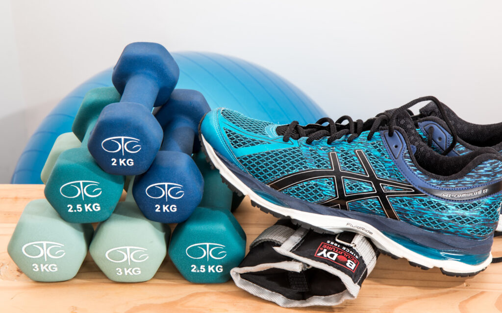 Ein blauer Turnschuh, Handelt und eine Gewichtsmanschette, im Hintergrund ein Gymnastikball