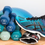 Ein blauer Turnschuh, Handelt und eine Gewichtsmanschette, im Hintergrund ein Gymnastikball