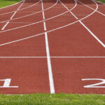 Eine Kunststoffbahn in der Farbe rot, dazu Markierungen für Läufer mit den Startnummern 1 bis 2, seitlich etwas Gras