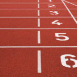 Eine Kunststoffbahn in der Farbe rot, dazu Markierungen für Läufer mit den Startnummern 1 bis 6