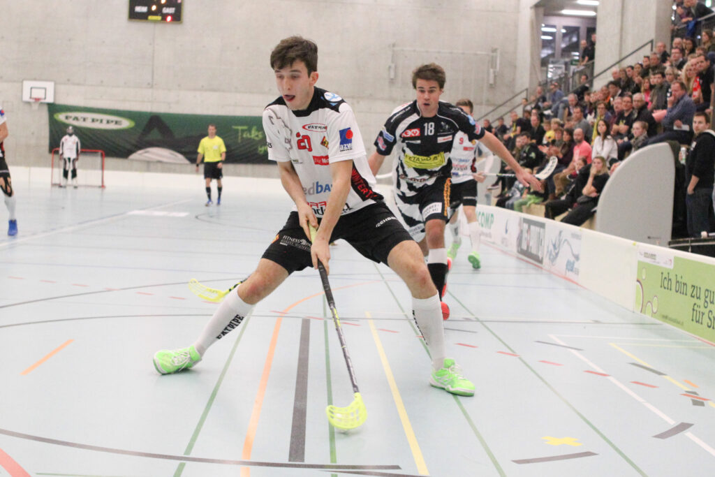 Mehrere Junge Männer einem Floorballspiel, dazu im Hintergrund Zuschauer