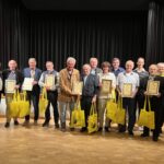 Eine Gruppe älterer Personen, die zuvor eine Urkunde überreicht bekommen haben, posieren für ein Gruppenbild