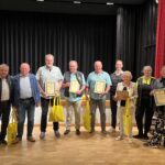 Eine Gruppe älterer Personen, die zuvor eine Urkunde überreicht bekommen haben, posieren für ein Gruppenbild