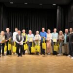 Eine Gruppe älterer Personen, die zuvor eine Urkunde überreicht bekommen haben, posieren für ein Gruppenbild