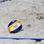 Ein Beachvolleyball liegt im Sand, dazu die Begrenzungslinien von einem Beachvolleyballfeld