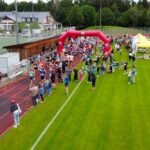 Der Start bei Grasbrunner Lauf 2024 mit vielen Kindern und Erwachsenen auf einer Kunststoffbahn, dazu ein aufgeblasenes Banner