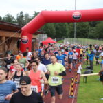 Der Start bei Grasbrunner Lauf 2024 mit vielen Kindern und Erwachsenen auf einer Kunststoffbahn, dazu ein aufgeblasenes Banner