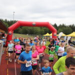 Der Start bei Grasbrunner Lauf 2024 mit vielen Kindern und Erwachsenen auf einer Kunststoffbahn, dazu ein aufgeblasenes Banner