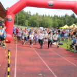 Der Start bei Grasbrunner Lauf 2024 mit vielen Kindern auf einer Kunststoffbahn, dazu ein aufgeblasenes Banner