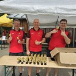 3 Männer vor einem Biertisch, darauf goldene Pokale