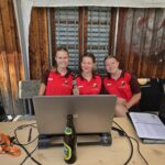 3 junge Mädchen sitzen auf Bank, davor steht auf einem Biertisch ein Laptop