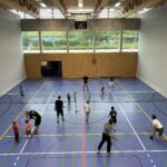 Ein Sporthalle mit zwei Badminton-Netzen und vielen Kindern und Jugendliche die Badminton spielen