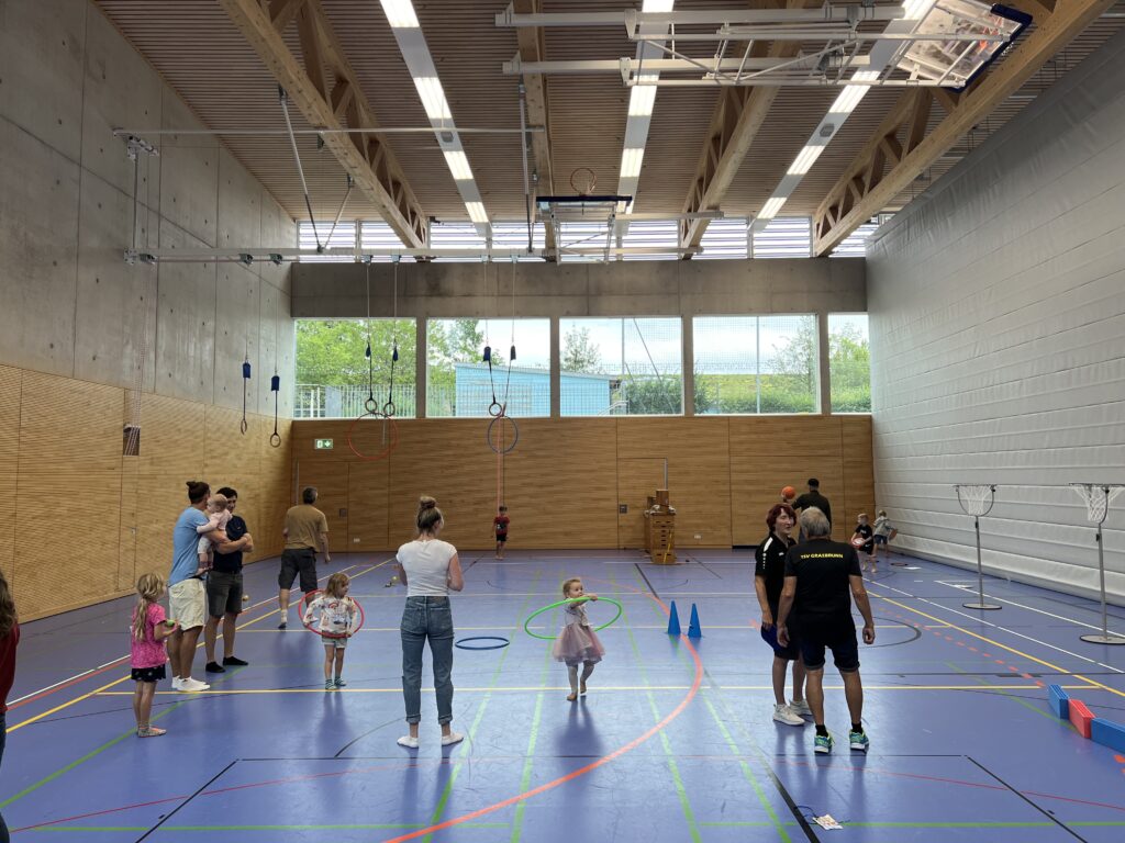 Eine Sporthalle mit vielen kleinen Kindern, die verschiedenen Ballspiele spielen und dazu einige Eltern