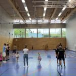 Eine Sporthalle mit vielen kleinen Kindern, die verschiedenen Ballspiele spielen und dazu einige Eltern