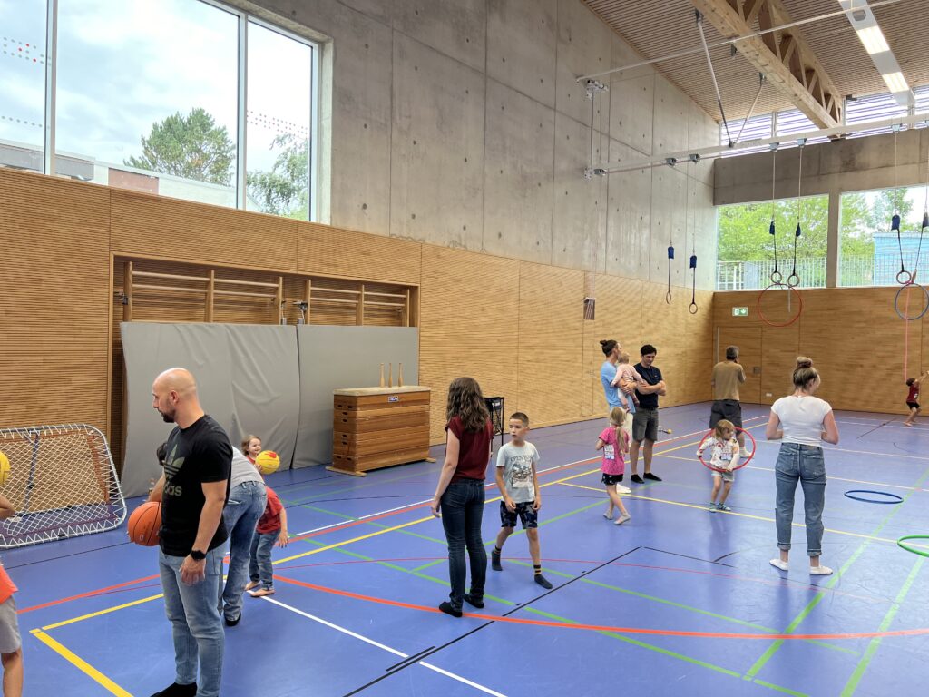 Eine Sporthalle mit vielen kleinen Kindern, die verschiedenen Ballspiele spielen und dazu einige Eltern