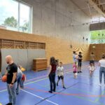 Eine Sporthalle mit vielen kleinen Kindern, die verschiedenen Ballspiele spielen und dazu einige Eltern