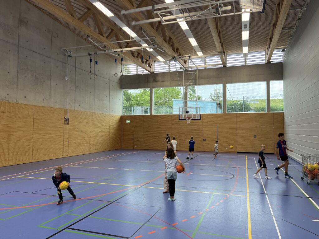 Eine Sporthalle mit vielen kleinen Kindern, die Basketball spielen und dazu einige Eltern