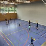 Eine Sporthalle mit vielen kleinen Kindern, die Basketball spielen und dazu einige Eltern
