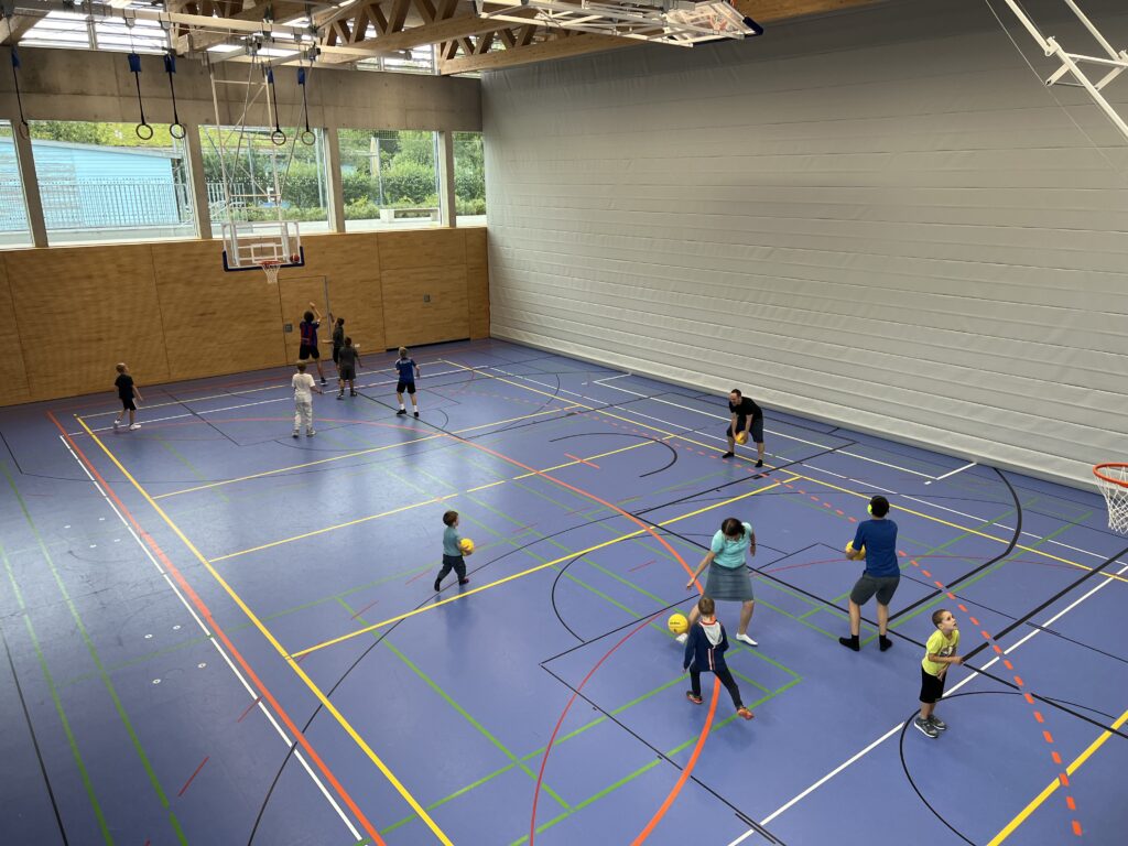 Eine Sporthalle mit vielen kleinen Kindern, die Basketball spielen und dazu einige Eltern