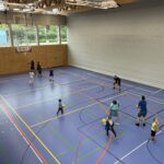 Eine Sporthalle mit vielen kleinen Kindern, die Basketball spielen und dazu einige Eltern