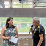 Eine junge, hübsche Frau mit einem Zettel in der Hand und ein Mann mit einem Mikrofon halten gemeinsam eine Rede