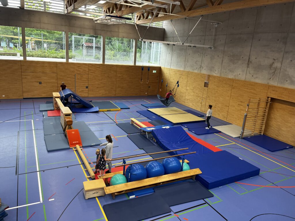 Eine Sporthalle mit einem Hindernisparcour, dazu viele kleine Kinder und einige Eltern