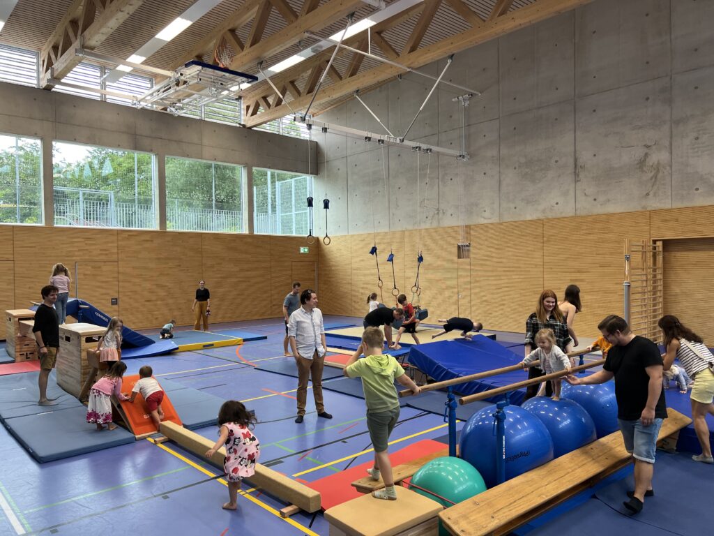 Eine Sporthalle mit einem Hindernisparcour, dazu viele kleine Kinder und einige Eltern