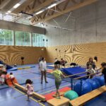 Eine Sporthalle mit einem Hindernisparcour, dazu viele kleine Kinder und einige Eltern
