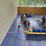 Eine Sporthalle mit einem Hindernisparcour, dazu viele kleine Kinder und einige Eltern