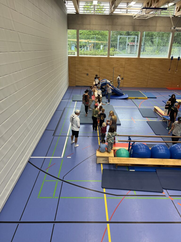 Eine Sporthalle mit einem Hindernisparcour, dazu viele kleine Kinder und einige Eltern