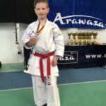 Ein Junge in einem Karateanzug, der eine Medaille in seiner Hand hält