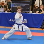 Ein Junge in einem Karateanzug mit blauem Gürtel, der ein Kampfschritt zeigt