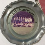 Ein Teller aus Blech, welcher an einer Wände hängt und ein Mannschaftsfoto zeigt