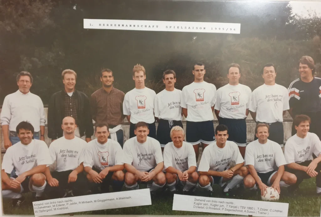 Ein altes Foto von einer einer Fußballmannschaft, dazu mehrere Trainer, im Hintergrund Bäume
