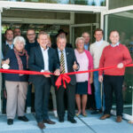 Viele Personen vor der Sporthalle Neukeferloh, dazu einen rotes Band, welches vom Bürgermeister mit einer Schere durchschnitt wird