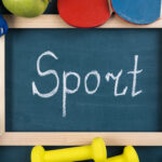 Tafel mit einem Holzrahmen mit dem Wort Sport mit einem Kreidestift geschrieben, außen herum verschiedenen Sportutensilien