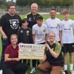 Mehrere Personen mit Paket in der Hand, im Hintergrund ein Fußballfeld