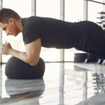 Junger Mann in einem Fitnessstudio mit schwarzen Haaren macht einen Plank auf einem Medizinball